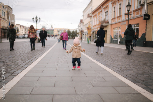 Happy baby girl walking in the city in autumn time. Cute baby in brown coat and jeans
