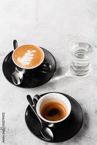 Two dark cups of hot black coffee, espresso, cappuccino with milk isolated on bright marble background. Overhead view, copy space. Advertising for cafe menu. Coffee shop menu. Vertical photo.