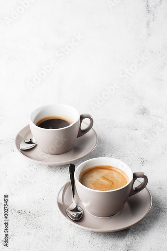 Two white cups of hot black coffee with milk isolated on bright marble background. Overhead view, copy space. Advertising for cafe menu. Coffee shop menu. Vertical photo.