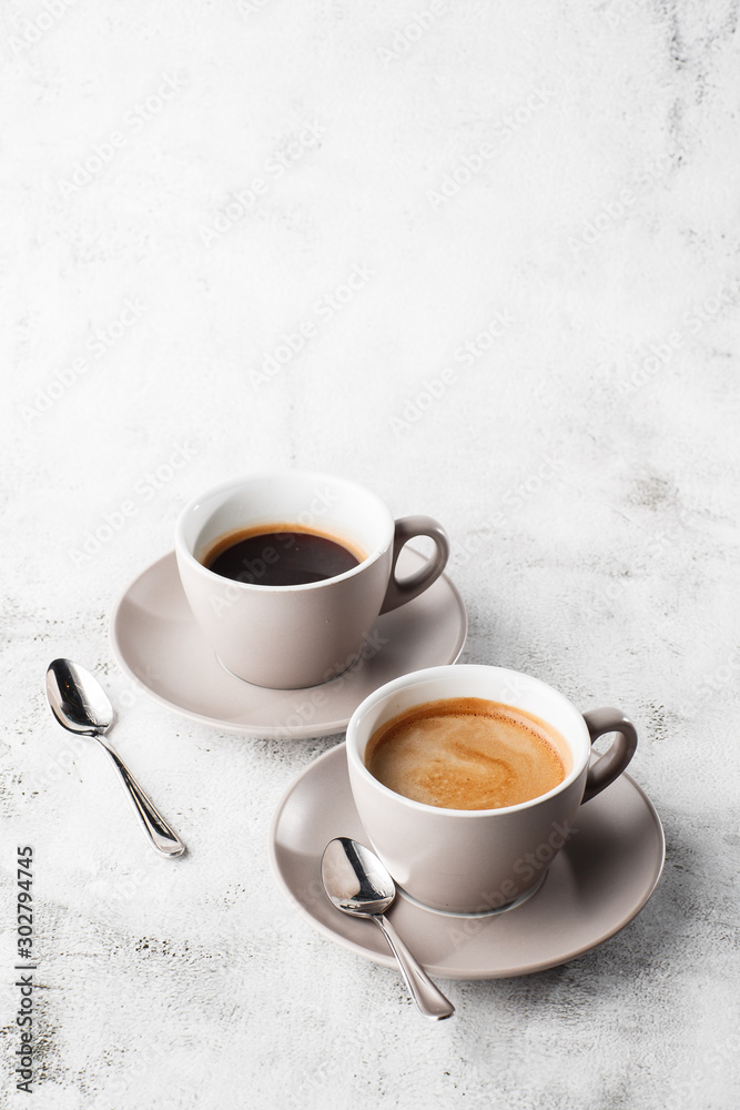 Two white cups of hot black coffee with milk isolated on bright marble background. Overhead view, copy space. Advertising for cafe menu. Coffee shop menu. Vertical photo.