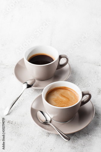 Two white cups of hot black coffee with milk isolated on bright marble background. Overhead view, copy space. Advertising for cafe menu. Coffee shop menu. Vertical photo. photo