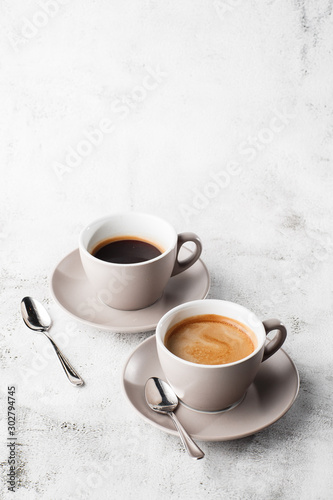 Obraz na płótnie Two white cups of hot black coffee with milk isolated on bright marble background. Overhead view, copy space. Advertising for cafe menu. Coffee shop menu. Vertical photo. w salonie