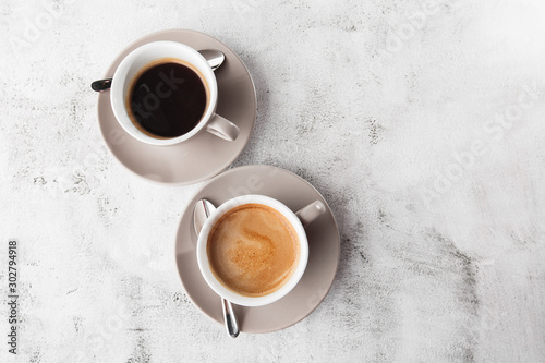 Two white cups of hot black coffee with milk isolated on bright marble background. Overhead view, copy space. Advertising for cafe menu. Coffee shop menu. Horizontal photo.