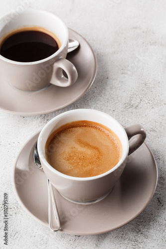 Two white cups of hot black coffee with milk isolated on bright marble background. Overhead view, copy space. Advertising for cafe menu. Coffee shop menu. Vertical photo.