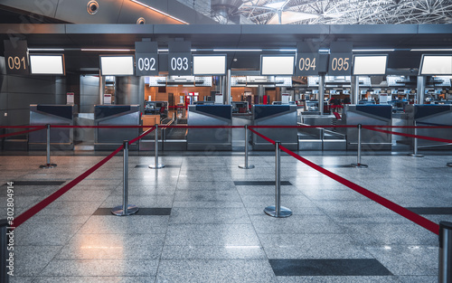 Front view of a check-in area in a modern airport: luggage accept terminals with baggage handling belt conveyor system, empty white information LCD screens mockups, indexed check-in desks, red ribbons