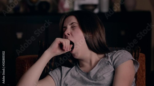 A young girl of European appearance is tired and yawns in an armchair at home. The concept of fatigue.
