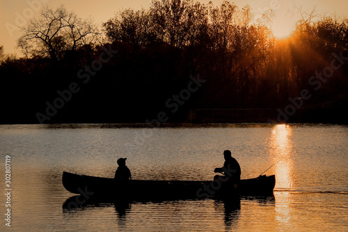 Close-Up Silhouette of a Man and a Child Together in a Canoe on a Lake in the Evening - with a Vibrant Orange Sunset in the Background