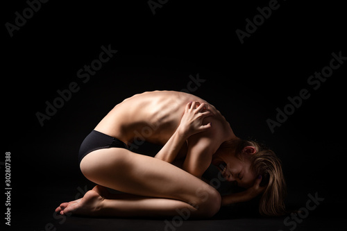 Helpless woman position embryo posing on a black isolated background. The concept of helplessness and loneliness. Female fear and hopelessness before fear and unchartedness