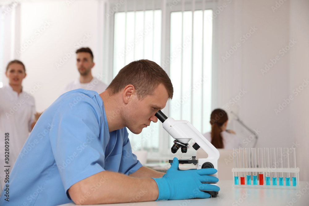 Scientist using microscope at table and colleagues in laboratory. Medical research Scientist using microscope at table and colleagues in laboratory. Medical research