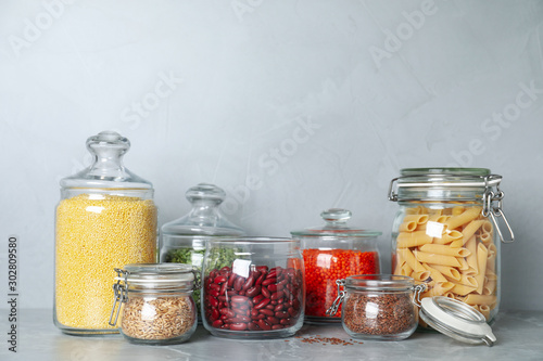 Glass jars with different types of groats on grey marble table