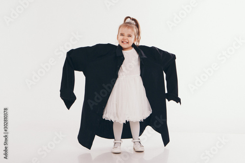 a little girl tries on dad's shirt. Child in big black clothes on white background. Concept of children's games, imitation of adult life, fashion