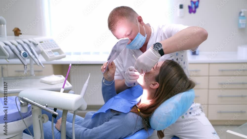 Female patient in dentist office. Dentist checking patient girl with mirror teeth up at dental clinic office Female patient in dentist office. Dentist checking patient girl with mirror teeth up at dental clinic office