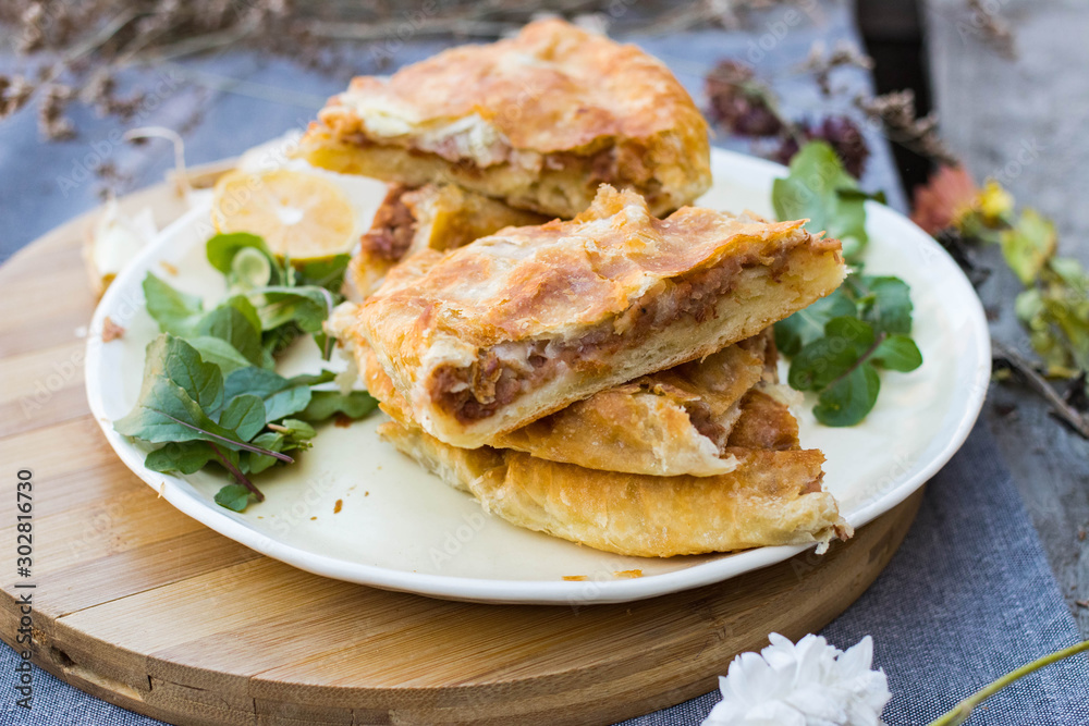 Lobiani - traditional baked Georgian pie with lobio beans and filo puff pastry. On plate with lemon slice, green rucola leaves and garlic. Homemade. Lobiani - traditional baked Georgian pie with lobio beans and filo puff pastry. On plate with lemon slice, green rucola leaves and garlic. Homemade.