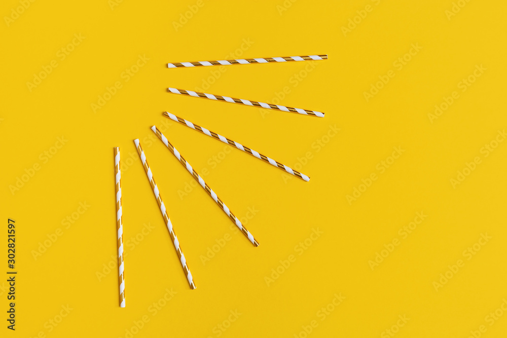 Bright paper straws for cocktail on yellow background with copy space. Summer Holiday concept. Abstract rays of sun. Minimal style flat lay.