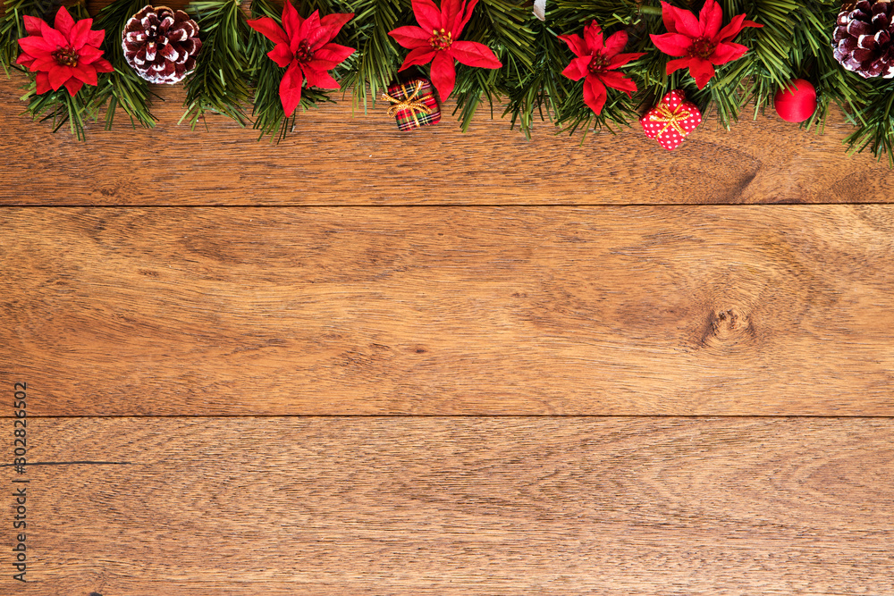 Christmas background with pine branches, red flowers, and cones on wooden board with copy space. Top view