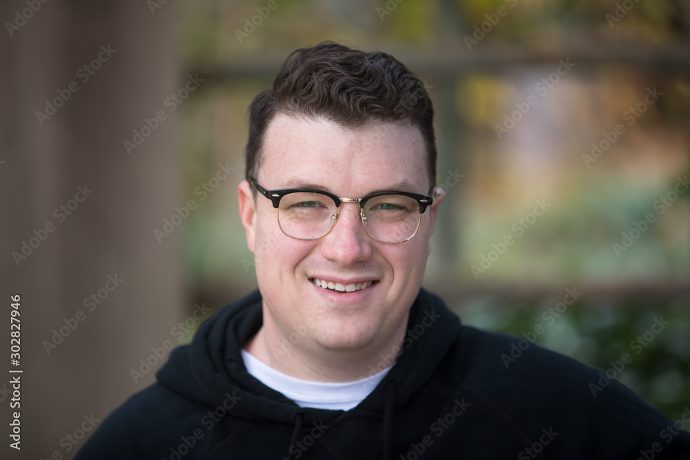 A caucasian male wearing a black hoodie sweater and glasses poses in a garden while surrounded by fall foliage on a cold afternoon. A caucasian male wearing a black hoodie sweater and glasses poses in a garden while surrounded by fall foliage on a cold afternoon.
