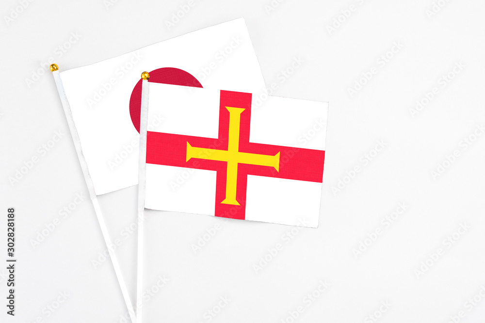 Guernsey and Japan stick flags on white background. High quality fabric, miniature national flag. Peaceful global concept.White floor for copy space.
