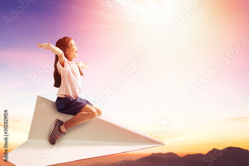 happy little girl on paper plane and flying in the sky