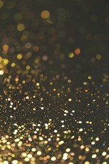 Golden bokeh background. Golden glitter on a black background.Festive New Year and Christmas shiny glitter layout.Vibrant background with twinkle lights. shiny gold