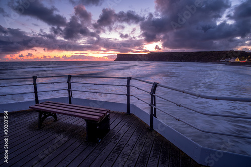 Wooden bench on pier overlooking tranquil sunrise at Saltburn by the sea