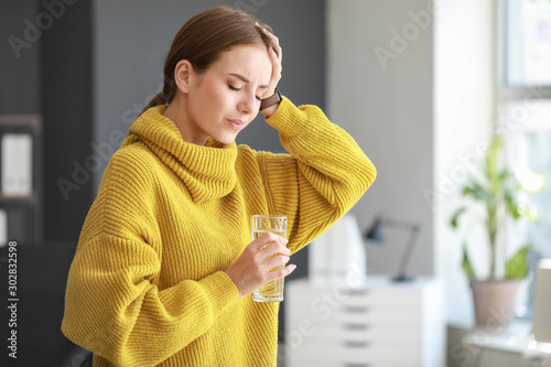 Young woman with glass of water suffering from headache at home photo