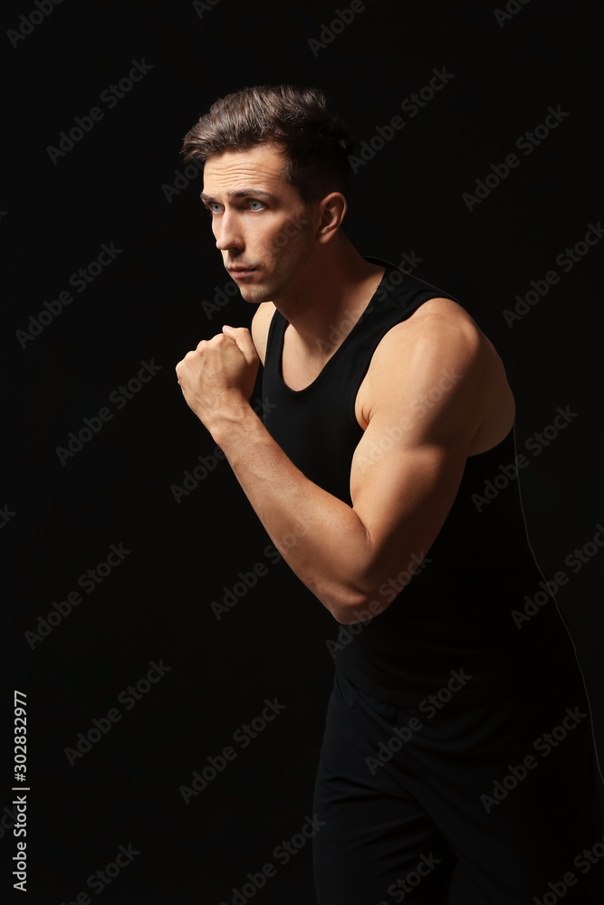 Sporty young man running against dark background