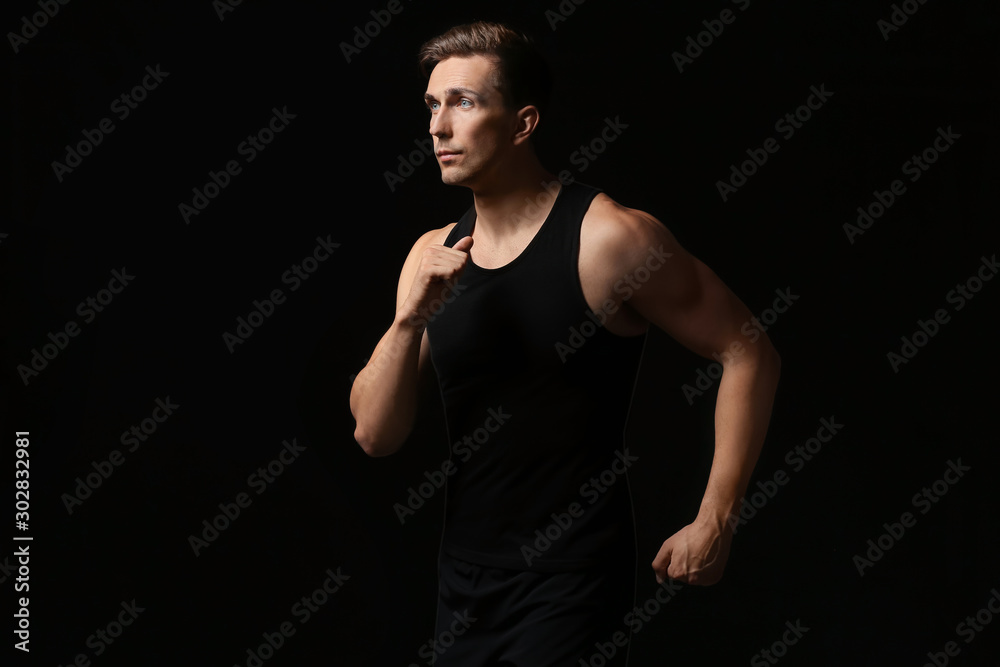 Naklejka premium Sporty young man running against dark background