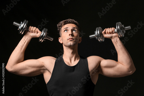 Sporty young man with dumbbells on dark background