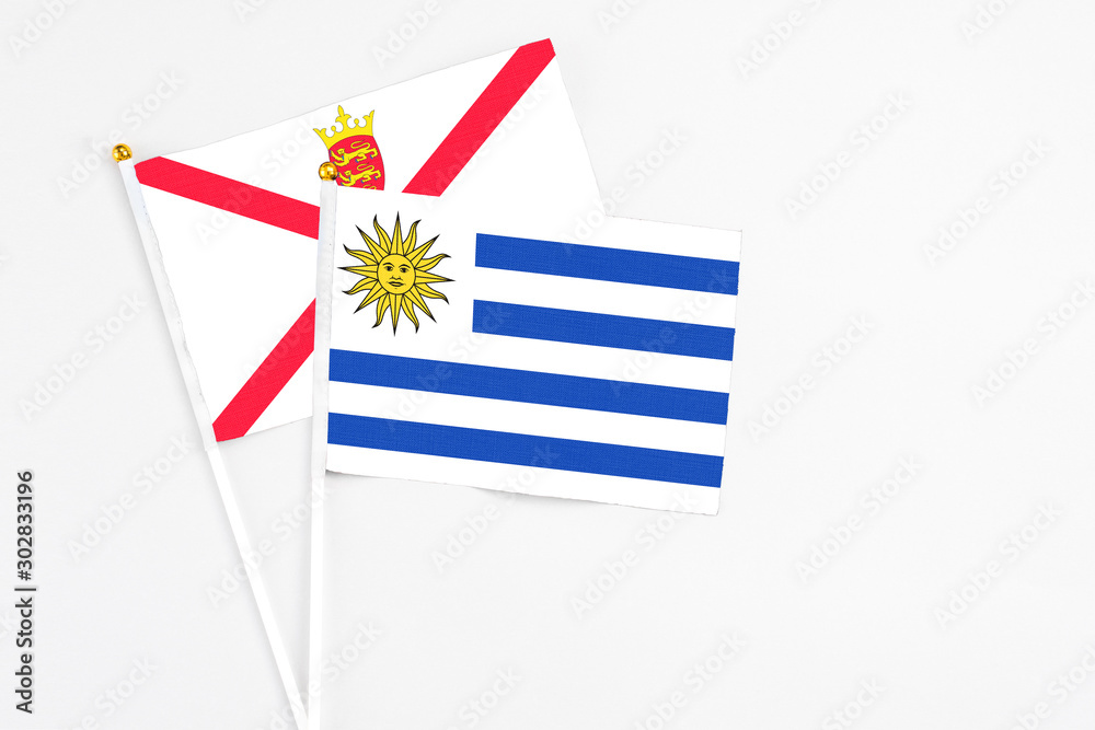 Fototapeta premium Uruguay and Jersey stick flags on white background. High quality fabric, miniature national flag. Peaceful global concept.White floor for copy space.
