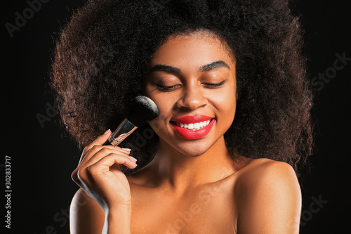 Portrait of beautiful African-American woman with makeup brush on dark background