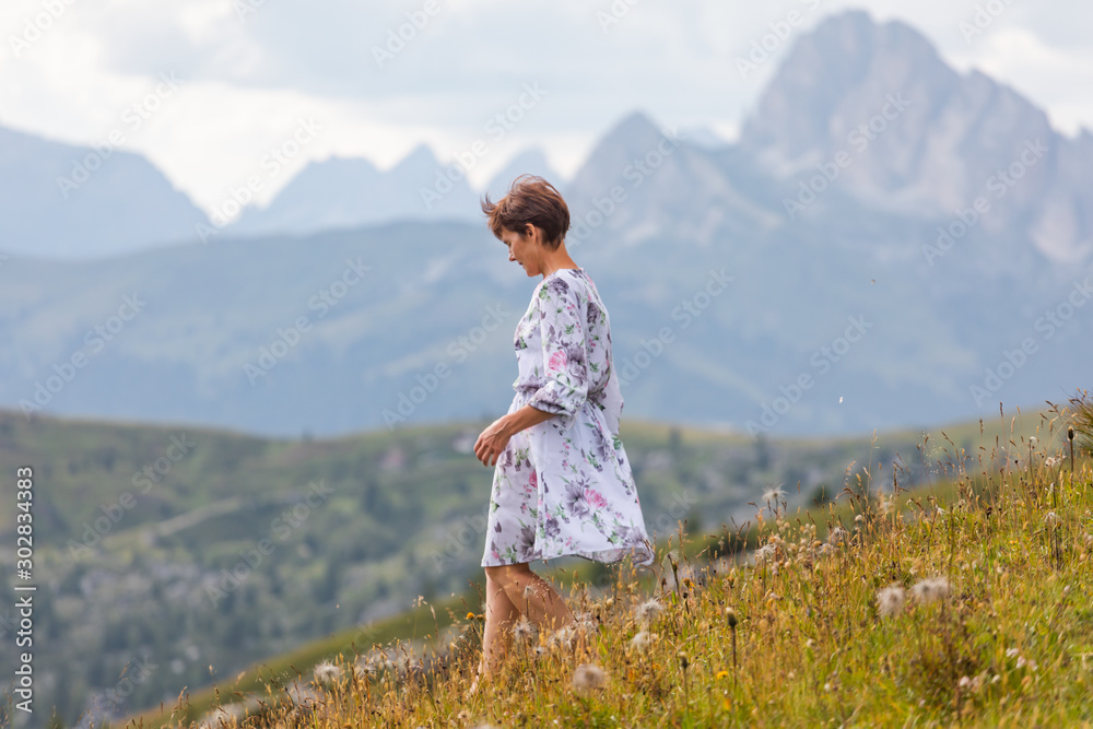 Fototapeta premium Girl in a dress on a background of mountains. Mountain valley of the Alps, Dolomites. Summer sunny day