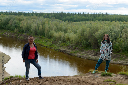 Two girls girlfriend Asian Yakut stand on the mountainside by the river in the taiga forest of Yakutia.