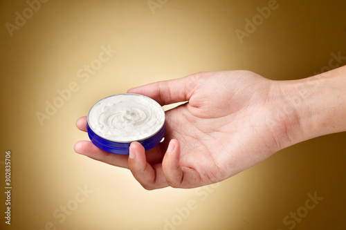 hand holding cream container on brown background, skin care concept