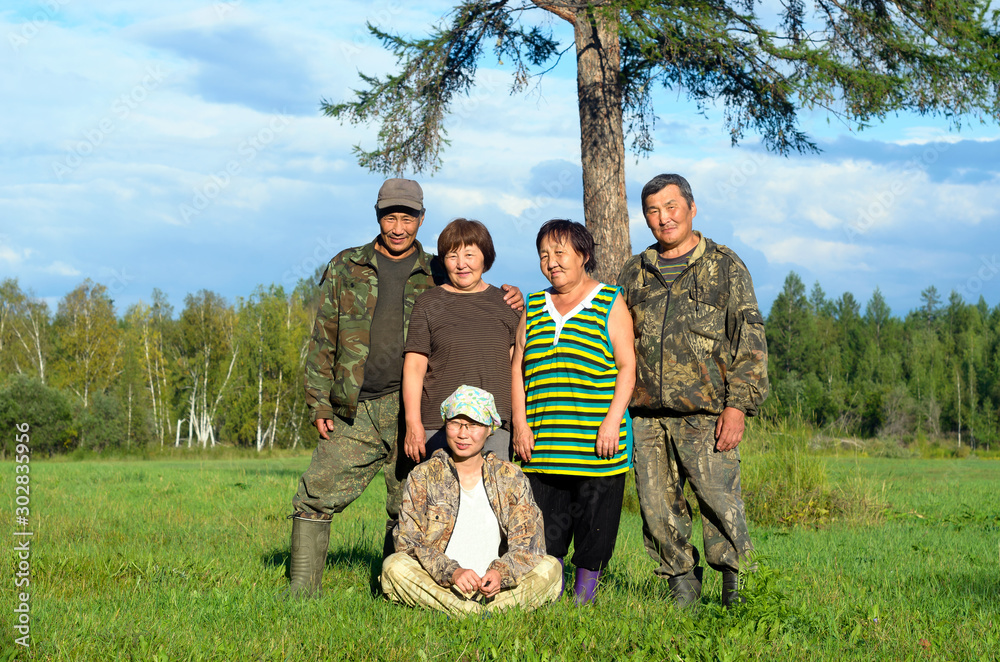 Obraz premium Two Yakut Asian elderly couples men and women with a young girl sitting on the grass pose for a family photo in a field near a tree.