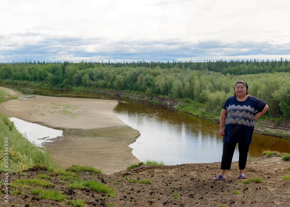 Full Yakut Asian girl posing for a photo stands on the edge of a cliff on the background of taiga forest and river in the North of Yakutia. Full Yakut Asian girl posing for a photo stands on the edge of a cliff on the background of taiga forest and river in the North of Yakutia.
