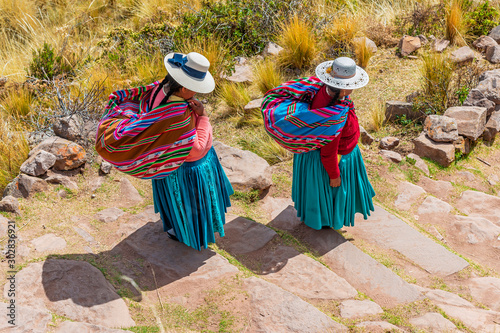 Obraz na plátně Two Quechua indigenous women in traditional clothing and textile walking down the steps on Taquile island by the Titicaca Lake, Puno, Peru