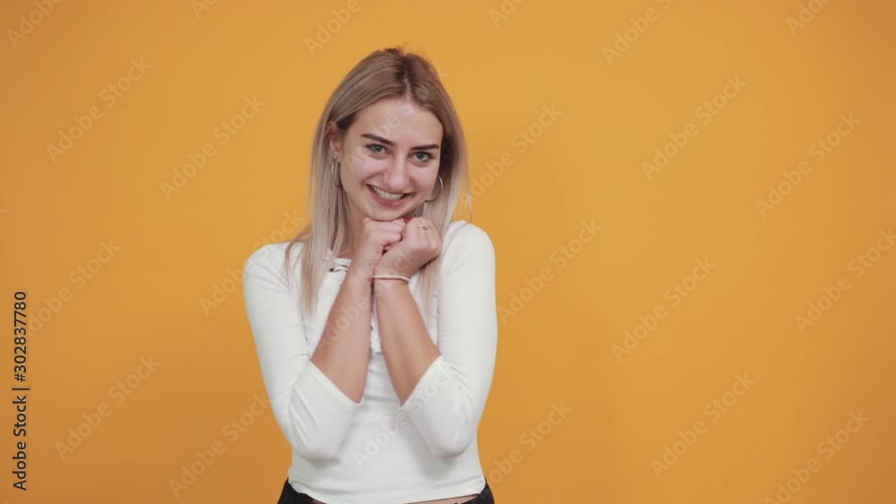 Young beautiful blonde woman wearing pastel white shirt looks happy and excited doing winner gesture keeping thumbs under chin. Celebration concept. Young beautiful blonde woman wearing pastel white shirt looks happy and excited doing winner gesture keeping thumbs under chin. Celebration concept.