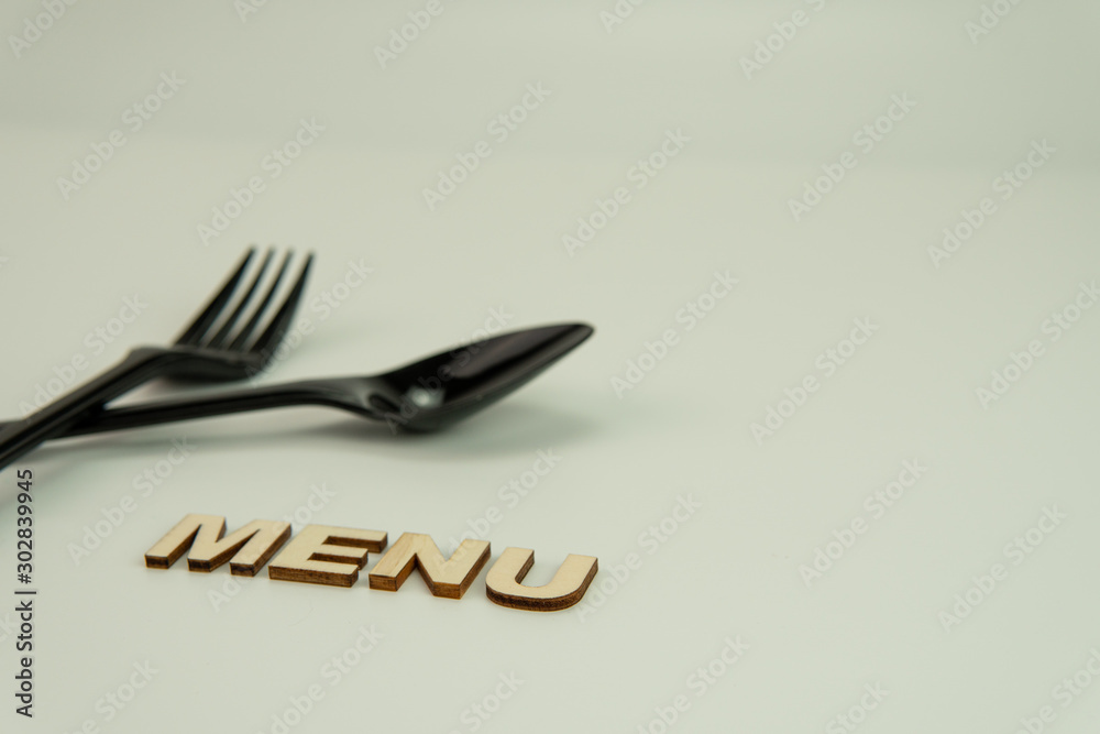 Selective focus of black shine spoon,fork and wooden alphabet word 'MENU' with white background. Food or restaurant concept. Selective focus of black shine spoon,fork and wooden alphabet word 'MENU' with white background. Food or restaurant concept.