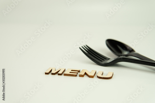 Selective focus of black shine spoon,fork and wooden alphabet word 'MENU' with white background. Food or restaurant concept. photo