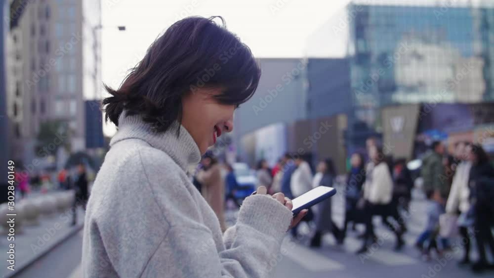 Side view slow motion of pretty asian woman holing mobile phone using smartphone walking across street busy urban business people commute browsing social media happy lifestyle