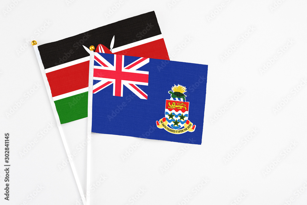 Fototapeta premium Cayman Islands and Kenya stick flags on white background. High quality fabric, miniature national flag. Peaceful global concept.White floor for copy space.