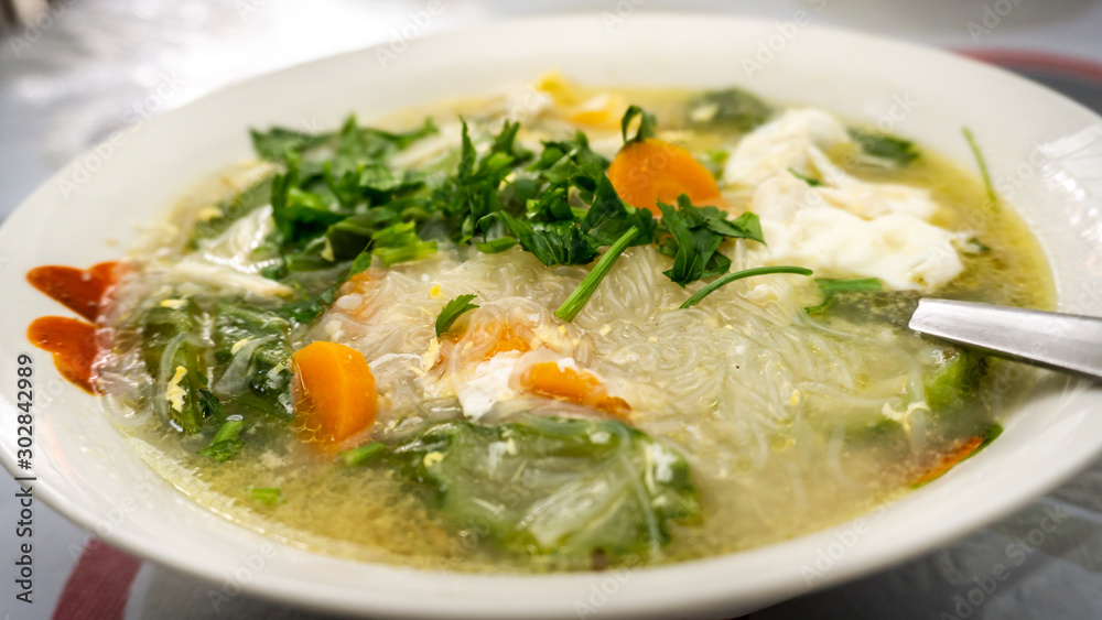 The close up view of the mixed vegetables soup with soo hoon noodles in a bowl.