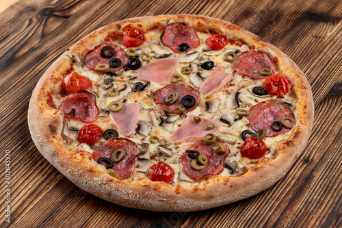 Hot meat pizza with pepperoni, salami, ham, melted cheese and olives on wooden table