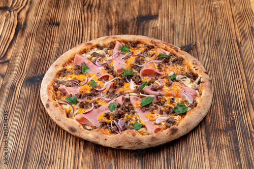 Pizza with minced meat and ham with cheese sauce on wooden table