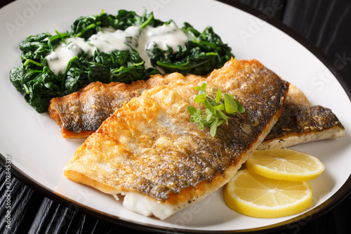 Serving fried sea bass fillet with spinach and lemon closeup on a plate. horizontal