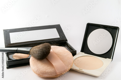 Composition of skin foundation and beauty accessories. Little mirror with powder and brushes isolated on white background.