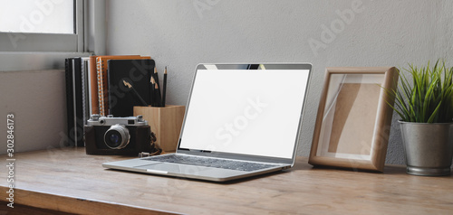 Cropped shot of comfortable workspace with blank screen laptop computer, office supplies and camera