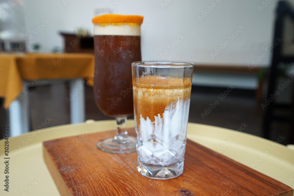 A glass of latte and iced black orange coffee on wooden tray A glass of latte and iced black orange coffee on wooden tray
