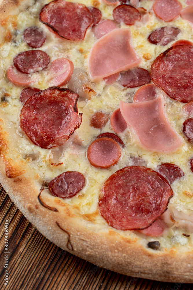 Close up of meat pizza with sausages, pepperoni, spicy chorizo and melted cheese on wooden table Close up of meat pizza with sausages, pepperoni, spicy chorizo and melted cheese on wooden table