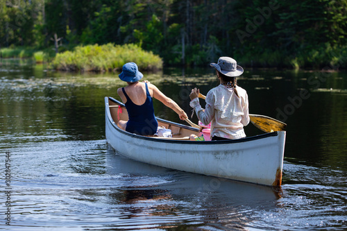 mother and daughter and the granddaughter are seen from the back as they riding small wooden boat and Rowing on the lake, with blurred trees on the background photo